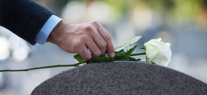 in a cemetery, a person places a flower on a gravestone of a victim of wrongful death
