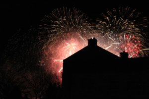Fireworks behind a house's dark silhouette.