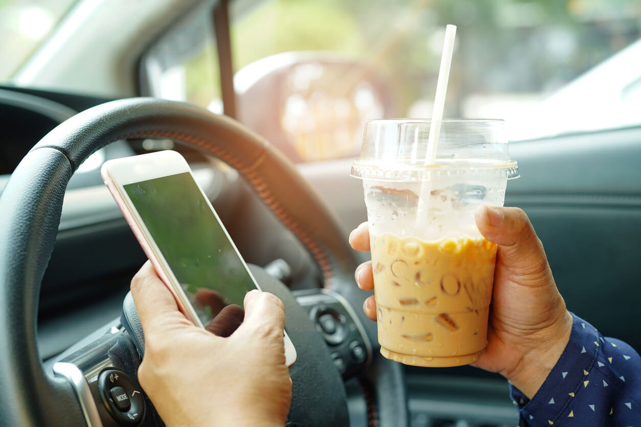 man driving with coffee in his hand and texting
